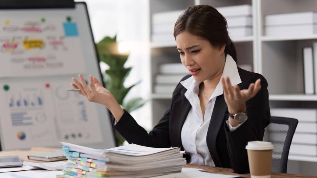 a woman sitting at a desk with a pile of papers